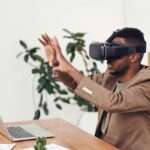 Man using a VR headset in an office with a laptop, representing metaverse and Web3 business tools